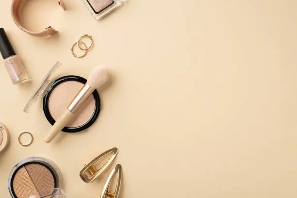 Makeup beauty concept. Top view photo of contouring palette gold rings bracelet barrettes makeup brush nail polish eyeshadow and compact powder on pastel beige background with empty space