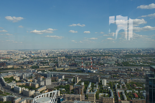 The view from above of modern Moscow city. Stalinist architecture. Wide photography. Summer day. Female face is reflected in the window. Photograph through window glass