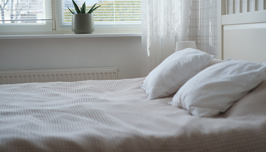 The interior of the room in white tones with a bed, bedside table, table lamp and a flower on the windowsill.