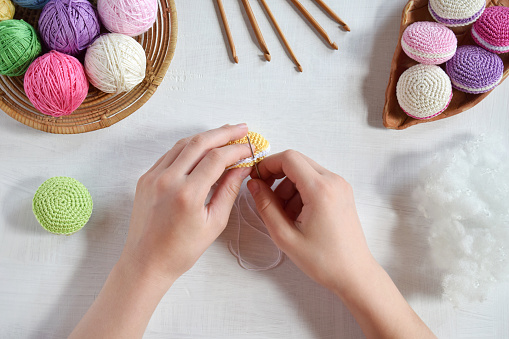 Making crochet amigurumi french macarons. Toy for babies or trinket.  Threads, needles, hook, cotton yarn. Handmade gift. Income from hobby. DIY crafts concept.  Step 3 - to sew all details.