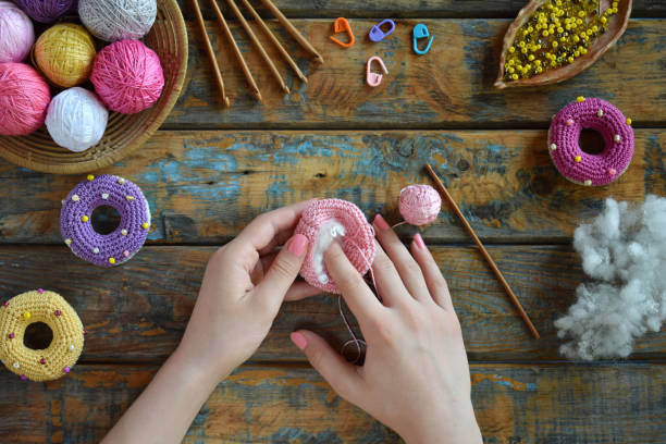 istock Making crochet amigurumi donuts. Toy for babies or trinket.  On the table threads, needles, hook, cotton yarn. Handmade gift. DIY crafts concept. Step 2. Stuff the toy with padding polyester. 1401000874