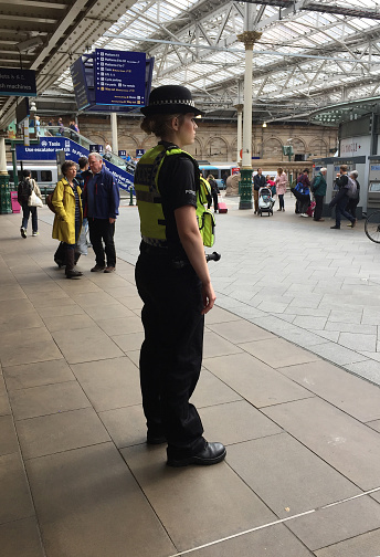 Edinburgh, Scotland - 06/11/2017:  Police woman standing at the train Edinburgh Waverley railway station,  the principal station. Police officer in service, maintaining order, helping people.