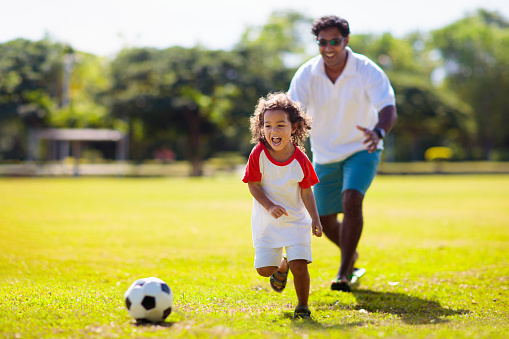 Father and son play football. Dad and little boy play soccer. Young active family enjoy sunny summer day outdoor. Healthy sport for kids. Football game club.