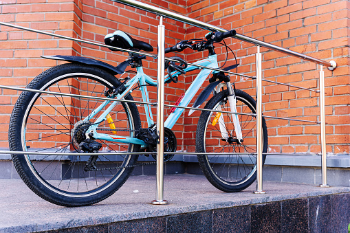a bicycle parked near the fence. the bike is tied with a bicycle lock to the fence on the background of a brick wall