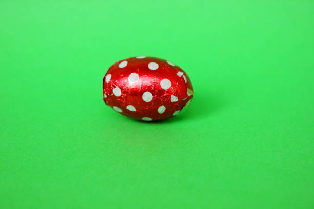 istock Chocolate egg in colorful foil for Easter on green background. The egg is wrapped in red foil. Happy Easter. Chocolate. Sweets for children and adults. Candy. Dessert. Copy space. Top view. Flat lay. 1401011089