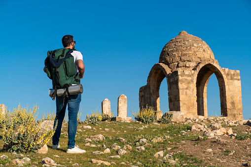 Backpacking man trekking in Dara Ruins in Mardin province. The young man visits the hill where the historical dome is located. Taken with a full-frame camera in sunny weather.