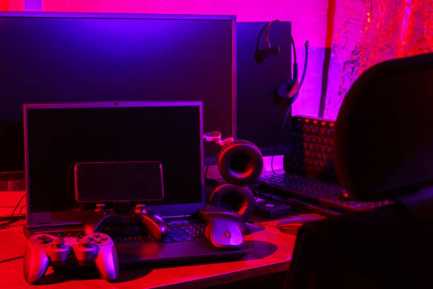 istock Gamer's workspace. Gamepads, computer mouse, headphones, keyboard and laptop on the table. Gaming accessories and computer equipment in neon light. Gambling addiction concept 1401016207