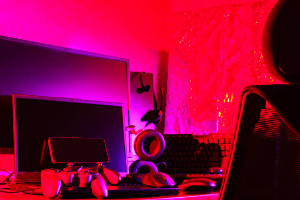 istock Video game controller, computer mouse, headphones, keyboard and laptop. Workspace with gaming accessories and computer equipment in neon light. Gamer work space concept 1401017015