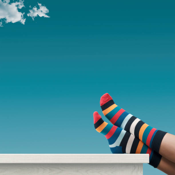 Creative carefree person wearing colorful striped socks and relaxing with feet up on the desk, blue sky in the background, blank copy space