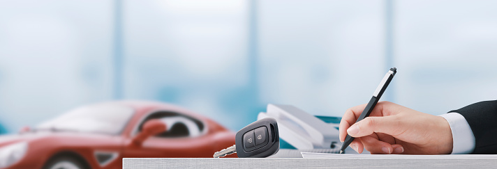 Car salesman writing a contract and luxury car in the background, car dealership concept