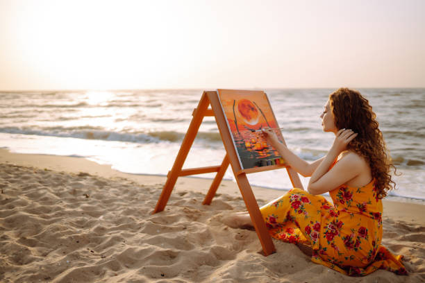 Young female artist drawing the picture at the beach. stock photo