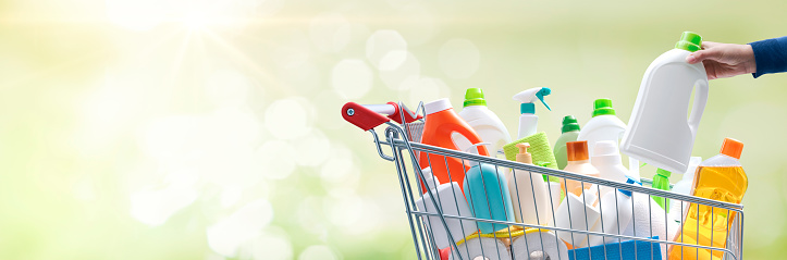 Woman putting a detergent bottle in a full shopping cart, hygiene and grocery shopping concept