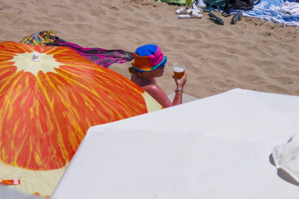Sunburnt woman wearing hat and drinking beer at the beach stock photo