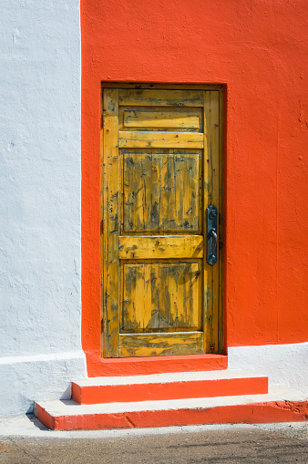 A weathered wooden door in a orange painted wall in St. George, Bermuda.