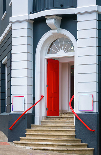 Red railings lead up a set of front stairs to a open red door with an arched window above.