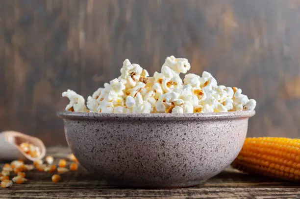 Photo of Freshly cooked popcorn in a bowl on a wooden table. Traditional American maize snack.