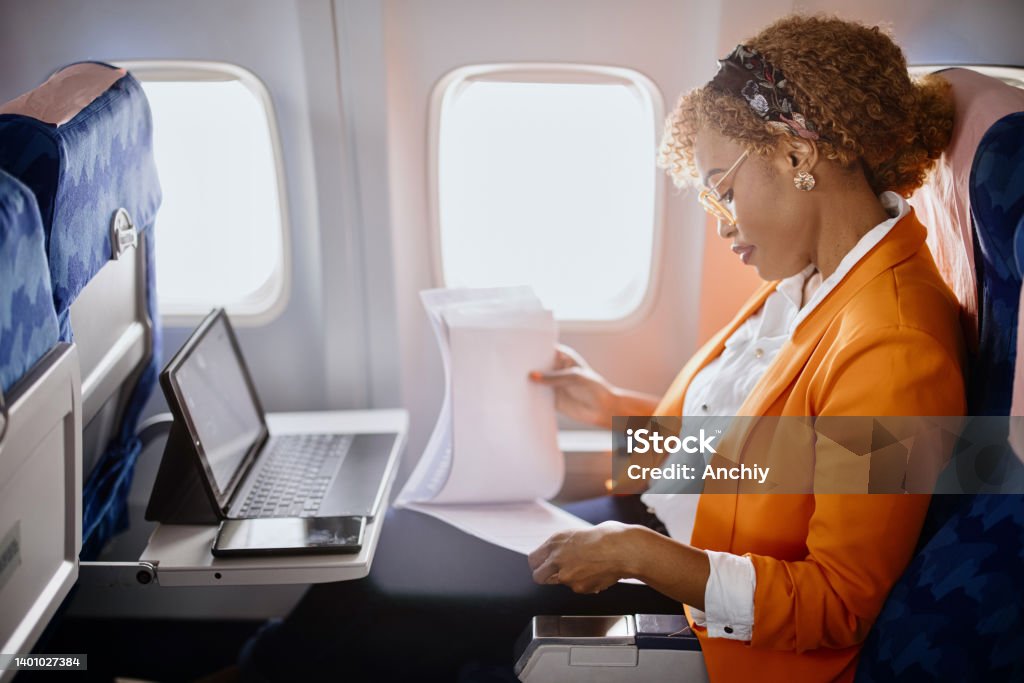 Businesswoman reading documents  and working on digital tablet during flight Business travel. Mature businesswoman sitting in an airplane using a laptop. Business Travel Stock Photo