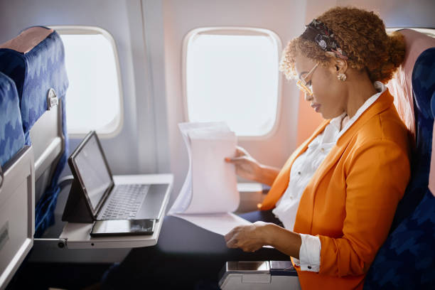 Businesswoman reading documents  and working on digital tablet during flight Business travel. Mature businesswoman sitting in an airplane using a laptop. business travel stock pictures, royalty-free photos & images