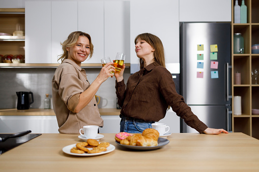 Two cheerful women in the kitchen with glasses of juice in their hands