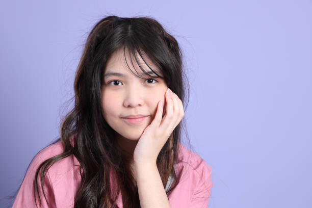 The cute young Asian girl with casual clothes standing on the purple background.