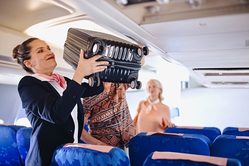 Cabin Crew helps passenger with putting bags and suitcases in overhead locker