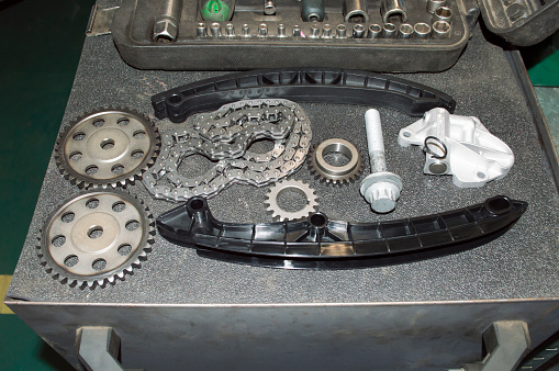 A complete new kit for replacing the timing chain of an automobile engine lies on a gray tool cart in an auto repair shop