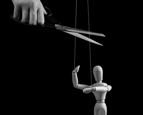 Hand cutting strings over puppet with scissors. Manipulation, negative influence, control stop concept. Overcoming addiction. Black and white. High quality photo