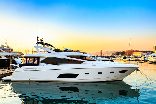 Luxury yacht docked in sea port at sunset. Motor boats and blue water. Relaxation and fashionable vacation.