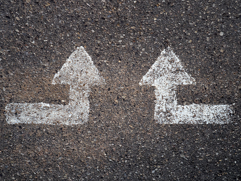 Top view of two white arrows in the asphalt of a road. Concept of guidance, lead and moving forward
