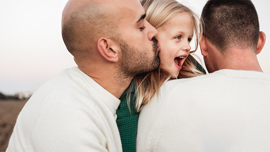 Gay male parents having tender moment kissing their son outdoor - Main focus on right father neck