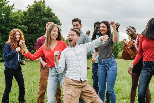 Multiethnic group of friends having fun dancing together outdoor during summer vacations - Focus on center man face
