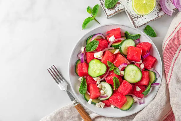 Summer fruit and vegetable salad made of watermelon, cucumber, soft cheese and onion on white table. Top view with copy space