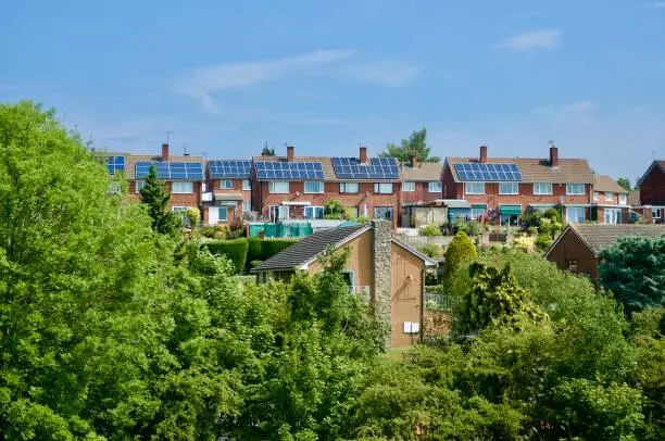 Village housing with solar panels on roof with trees in foreground.