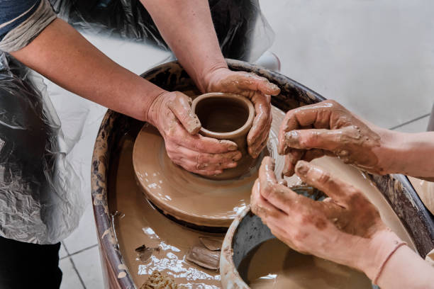 Hands of senior woman and girl sculpting clay vase on potter's wheel at pottery training lesson. Hands of senior woman sculpting clay vase on potter's wheel at pottery training lesson. Hands of girl craftswoman, teaching pottery craft. Hobby concept homemade pottery wheel stock pictures, royalty-free photos & images