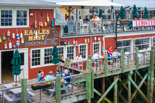 Bar Harbor, Maine, USA- May 26, 2022- Tourists, visitors and families enjoy a seafood lunch on both levels of an outdoor deck along the waterfront of Bar Harbor, Maine on a late May afternoon.