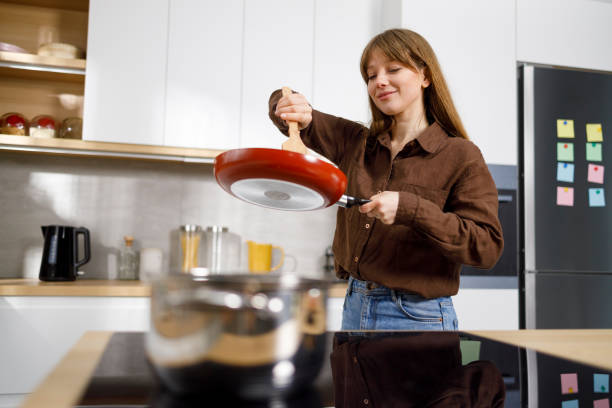 young woman at the stove stirring food in a frying pan with a spatula. housewife cooks in the kitchen - pan frying pan fried saucepan imagens e fotografias de stock
