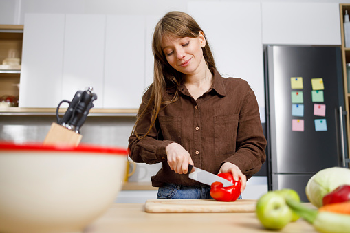 Young woman cutting paprika in the kitchen. Housewife preparing food
