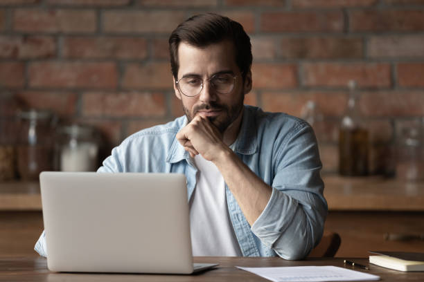 istock Thoughtful focused man in glasses looking at laptop screen 1401047204
