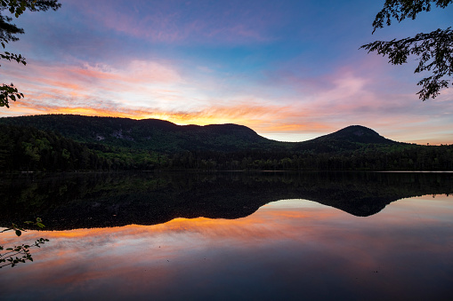 Warm morning sunrise behind a calm pond and the White Mountains of New Hampshire.