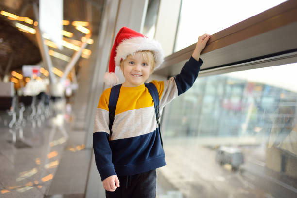 Little child wearing Santa Claus hat on background of an international airport. Preschooler boy is waiting for a merry Christmas.. Family trip for winter holidays. Kids vacation. stock photo