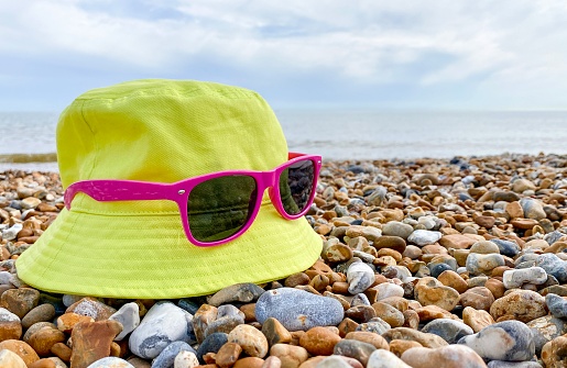 Bright summer hat with sunglasses on a pebble beach near the sea. Picture can be used as copy space or background.