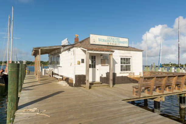 A dock off of Ocracoke's Community Square on Silver Lake. Ocracoke, North Carolina, August 15, 2021 - A dock off of Ocracoke's Community Square includes the Ocracoke Working Waterman's Exhibit and access to boats for tours of Silver Lake and Pamlico Sound. ocracoke island stock pictures, royalty-free photos & images