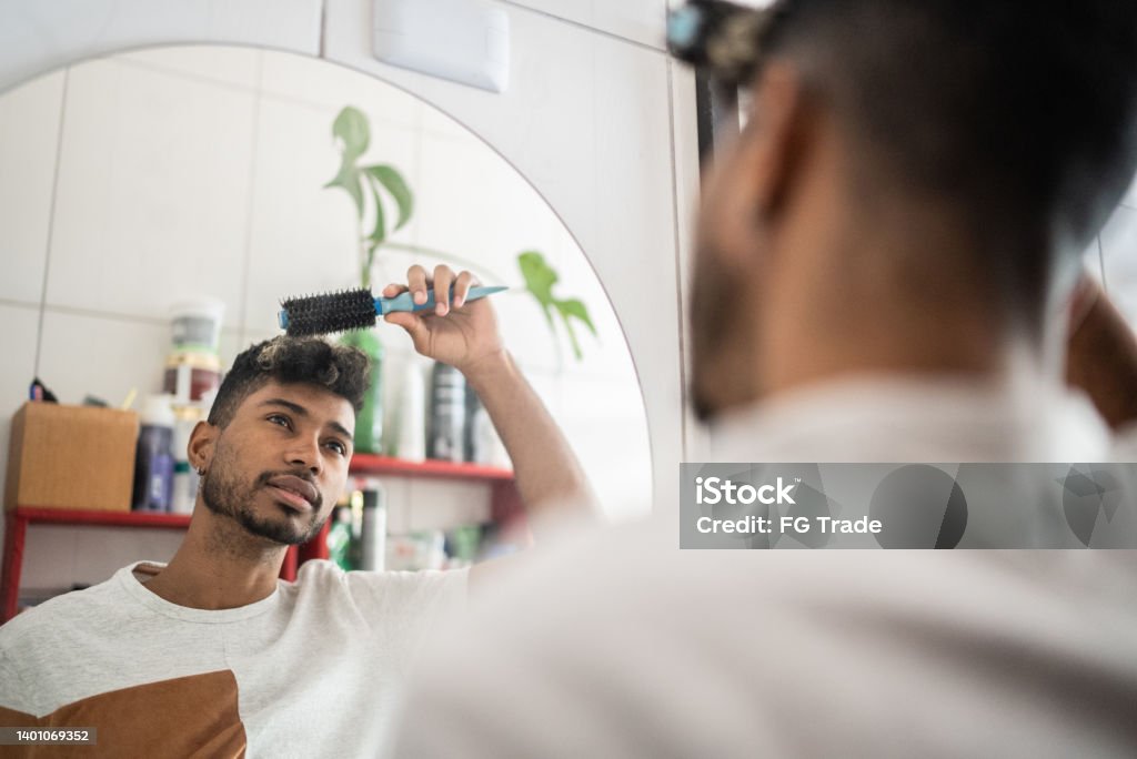 Young man brushing hair with comb at bathroom Mirror - Object Stock Photo