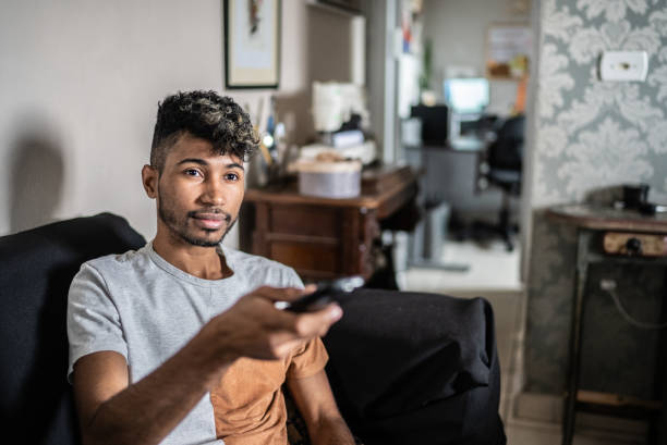 Young man using remote control while watching TV at home