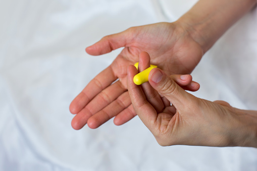 Close up of female hands and yellow foam earplugs. Woman taking the antinoise earplug. Light background.