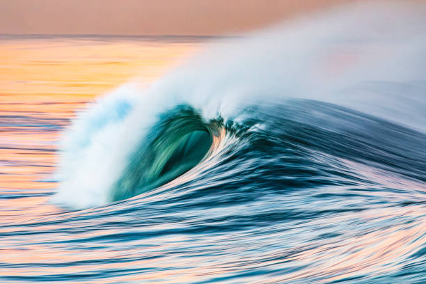 istock Curved pastel ocean wave reflecting a bright golden sunset at the beach 1401072091