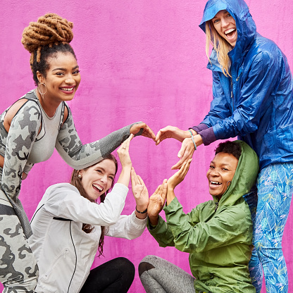 Portrait of a group of happy multiracial female friends making a heart shape with their hands against purple background