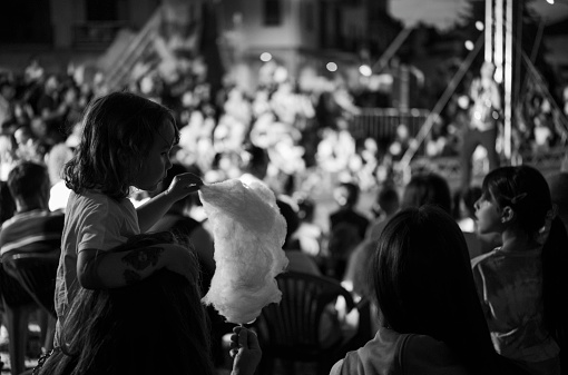 Parabiago, Italy - June 04, 2022: a little girl is eating cotton candy during a free circus show. scene portrayed in the square in the center of Parabiago