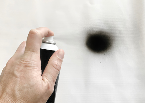Closeup of a man spraying black spray paint on a white surface.