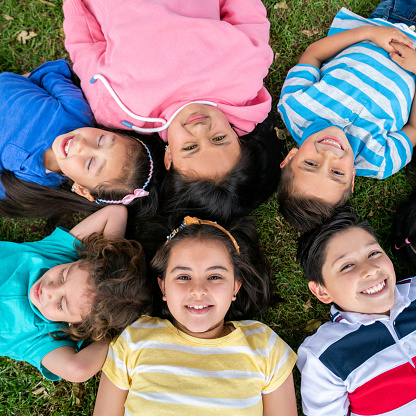 Happy group of Latin American kids lying on the floor in a circle and looking at the camera smiling